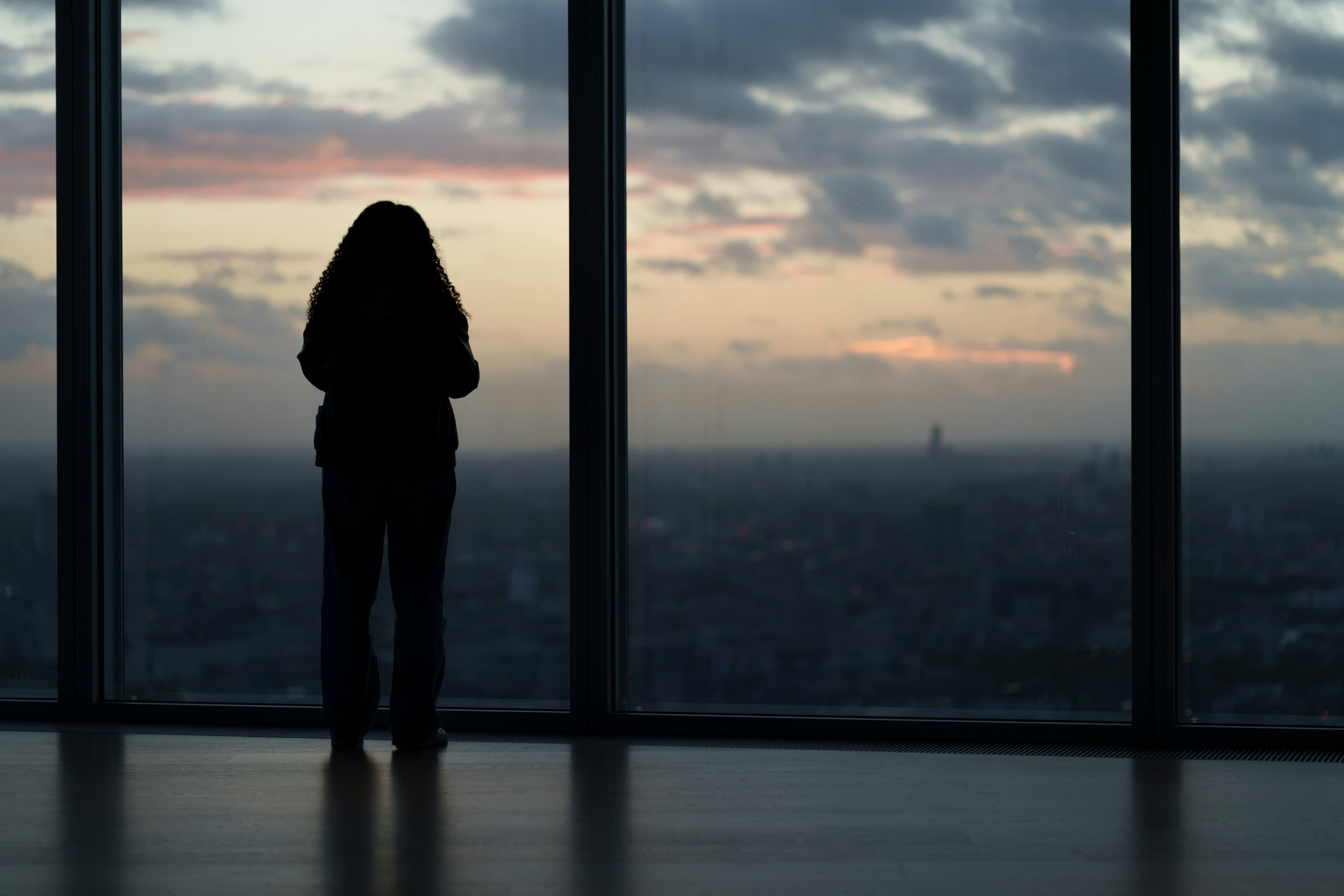 Silhouette d’une personne devant une grande baie vitrée au crépuscule, vue sur la ville