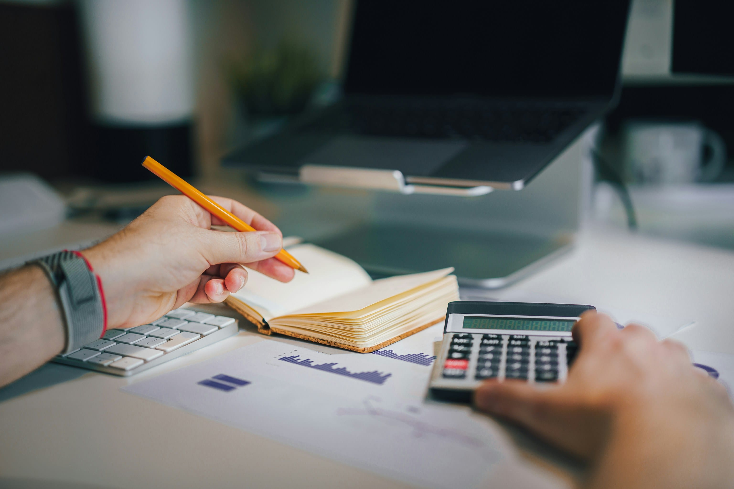 Main prenant des notes à côté d’une calculatrice et d’un ordinateur